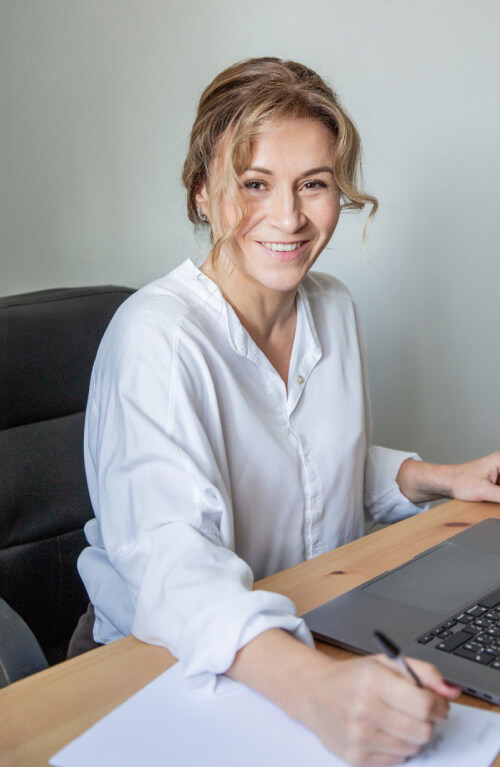 Coach professionista sorridente al lavoro con laptop, simbolo di professionalità e approccio positivo al coaching.